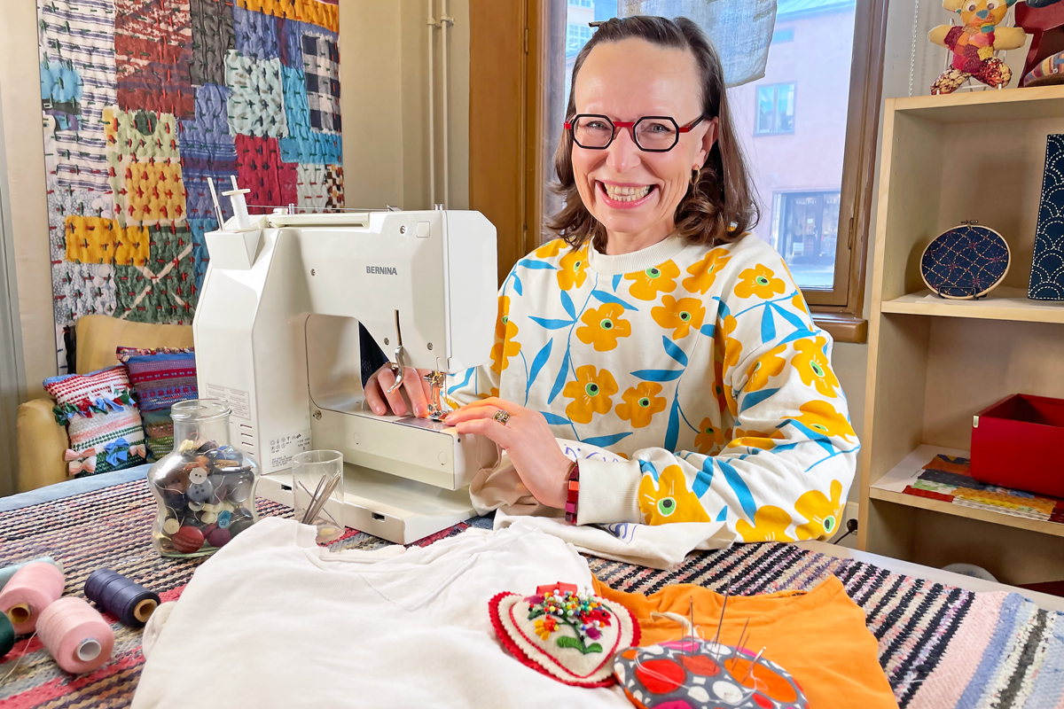 Tikkitaituri Sirke Lohtaja-Ahonen korjaamassa kangaskassia ompelukoneella Taito Shop Turun pop-up- tilassa ympärillään kaikkea korjaukseen, paikkaukseen ja kunnostukseen liittyvää materiaalia ja tarvikkeita.