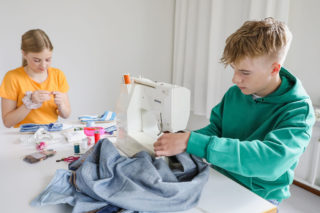 Teinikäinen tyttö ja poika korjaavat vaatteita ompelukoneella.