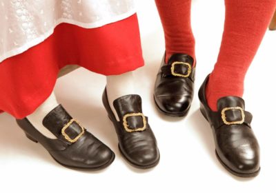 Kansallispuvun neulotut sukat, valkoiset ja punaiset, jalassa solkikengät.