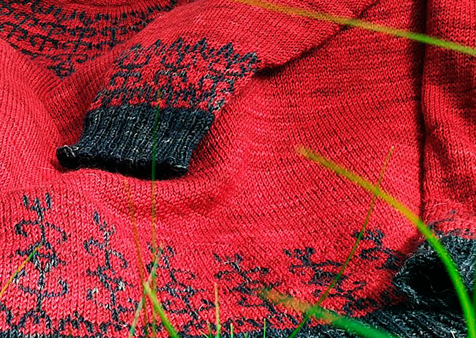 Punainen villapaita, jossa mustia karjalaistyylisiä kuvioita.