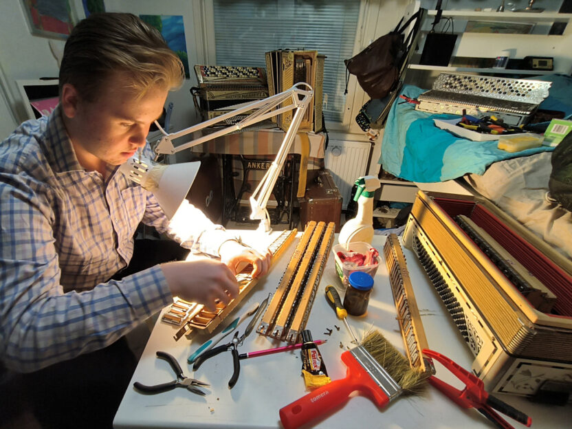 15-vuotias Petu Partanen soitinkorjauspöydän ääressä tekemässä korjaustyötä, pöydällä haitarin osia ja työkaluja.