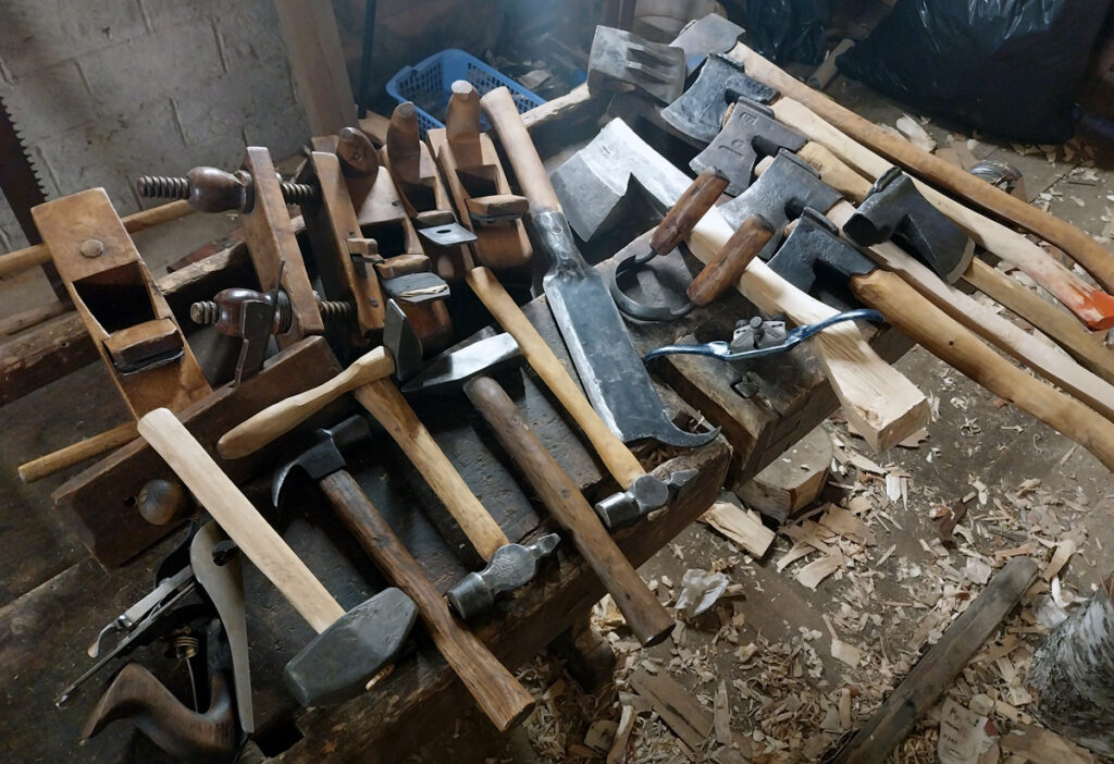 Vanhoja puuvartisia työkaluja pöydällä, vasaroita, kirveitä ja höyliä.