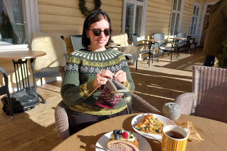 Nuori nainen villapaidassa neuloo aurinkoisella kuistilla Taitokorttelissa