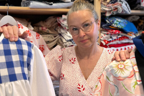 Maria-Söderström seisoo kangashyllyn edessä, kahden mallinukketorson välissä.