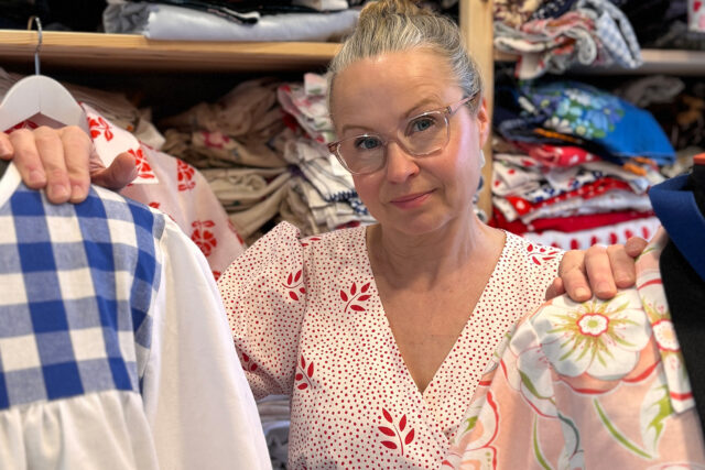Maria-Söderström seisoo kangashyllyn edessä, kahden mallinukketorson välissä.