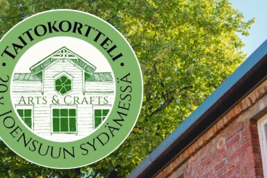 Taitokortteli 20 vuotta Joensuun sydämessä logo kesäisellä Taitokortteli-taustalla. Kuvassa Taitokorttelin tiilitalo ja vihreä lehmus