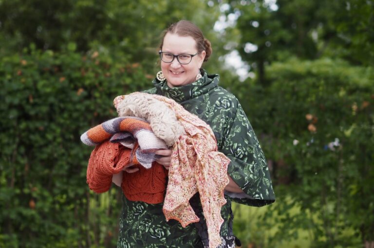 Iloinen nainen pitää käsissään erilaisia neuleita.