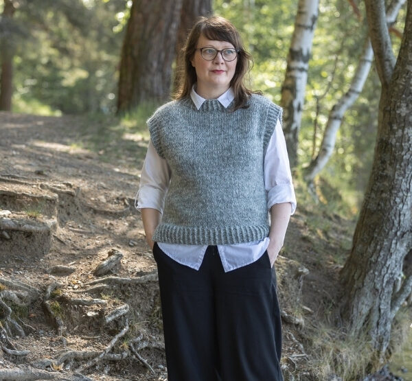 Harmaa Hanki-neuleliivi naisen päällä kuvattuna metsässä.